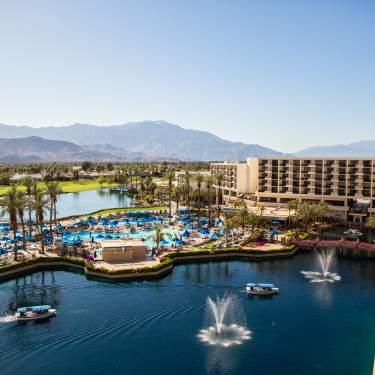 Aerial view of lake by resort and mountains in background with blue sky