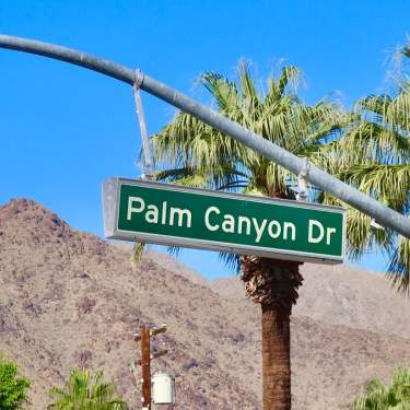Green Palm Canyon Drive street sign with mountain and palm tree background.