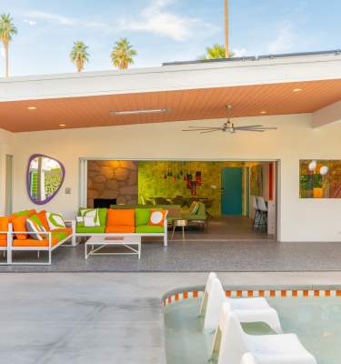 Palm Springs Vacation Rental modern patio with colorful seating, a pool, and a bright interior view featuring vibrant decor.