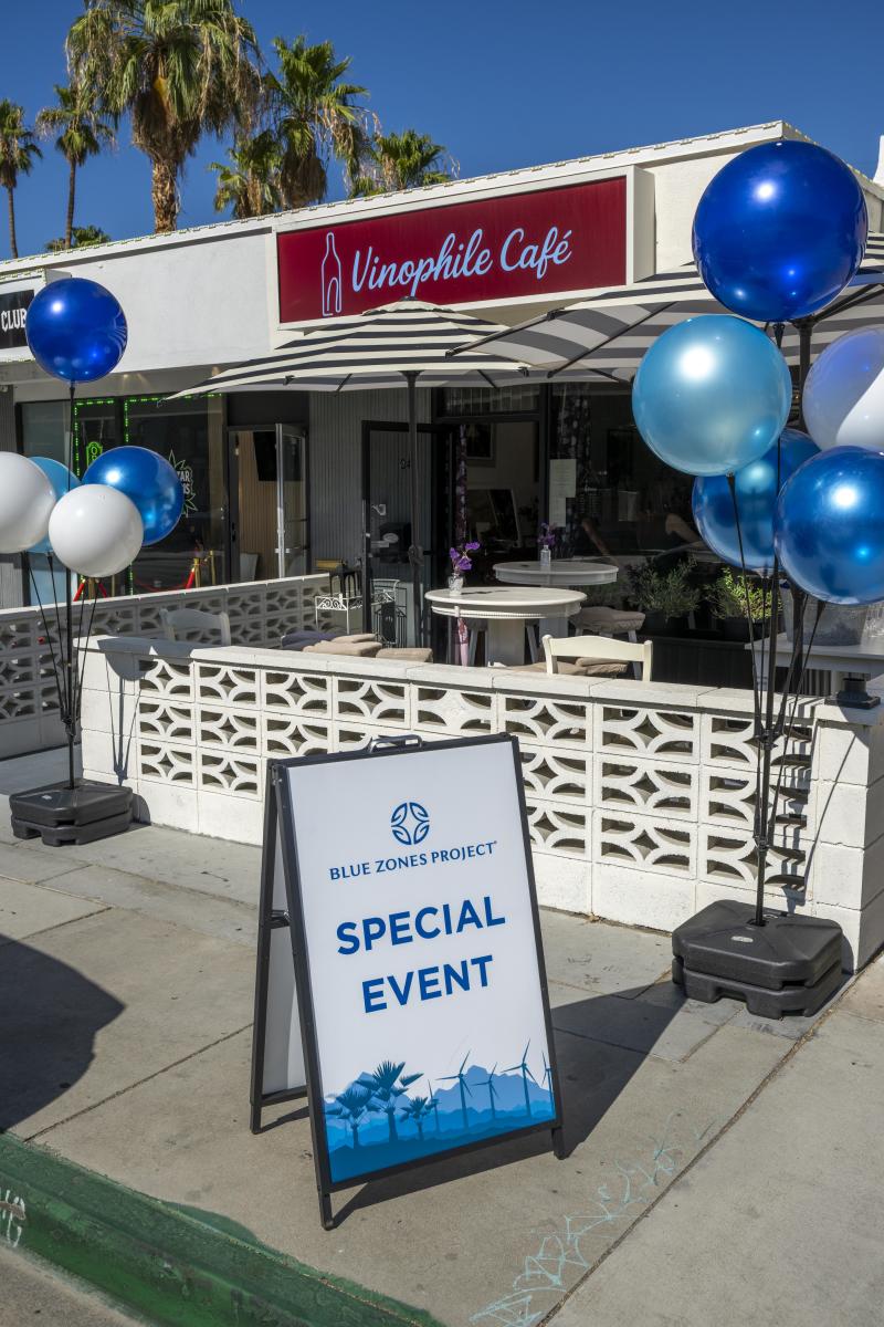 A shot of the exterior of Vinophile Cafe with blue balloons and a special event sandwich board provided by Blue Zones.