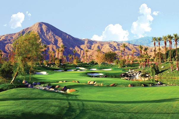 Green golf course against mountains and palm trees