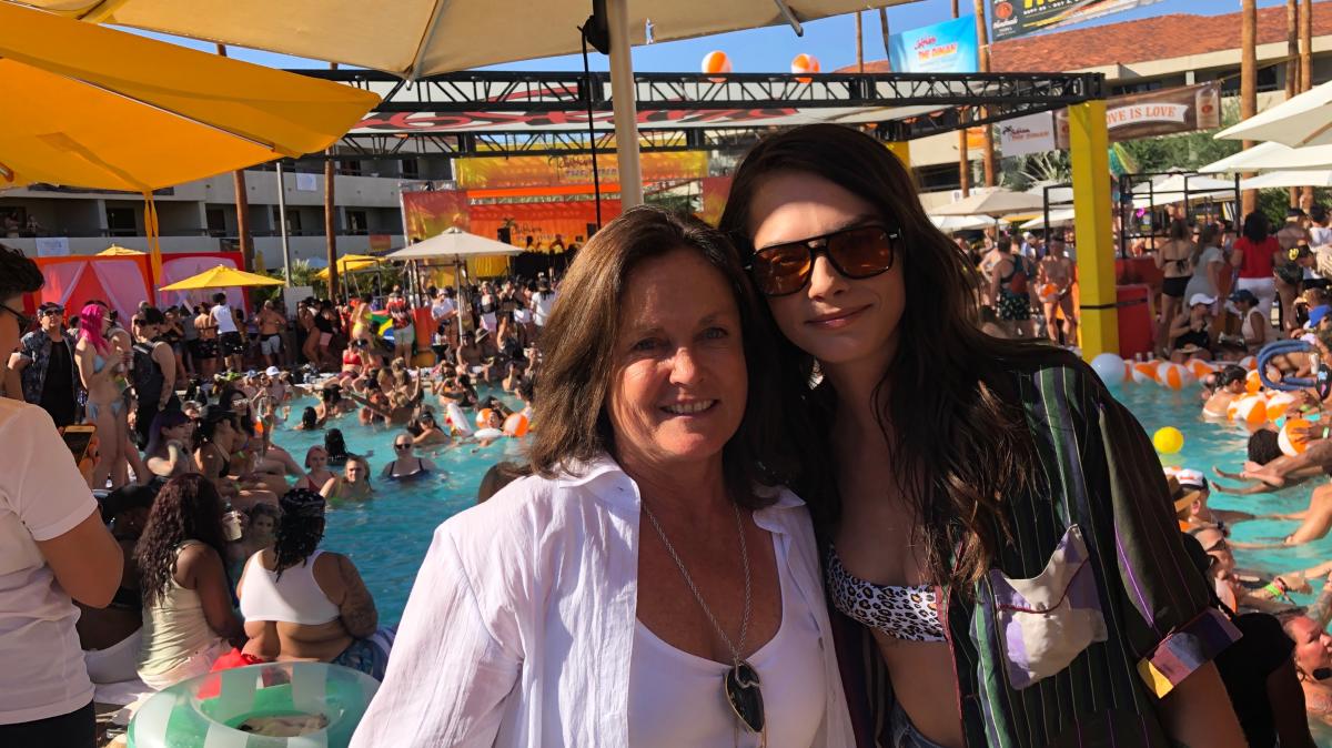 The Dinah founder Maria Hanson and actress/model Cara Delevingne pose for a picture in the foreground with a pool party behind them.