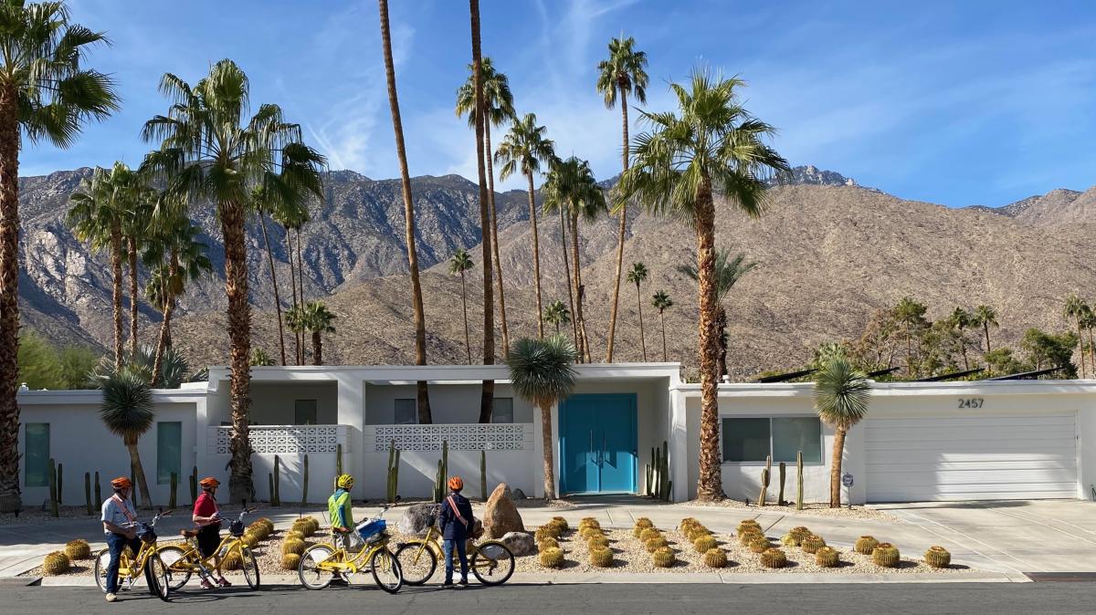 People are on their bike in front of a home in Palm Springs with the mountains in the background.