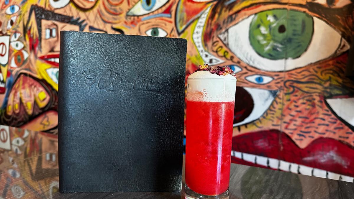 A cocktail sits on a table with colorful artwork in the background at Clandestino restaurant.