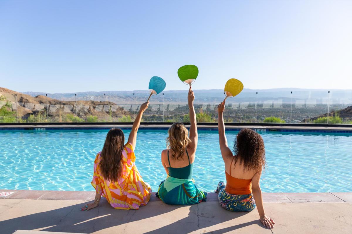 Three girl friends holding up fans and posing for a photo poolside at The Ritz-Carlton, Rancho Mirage.