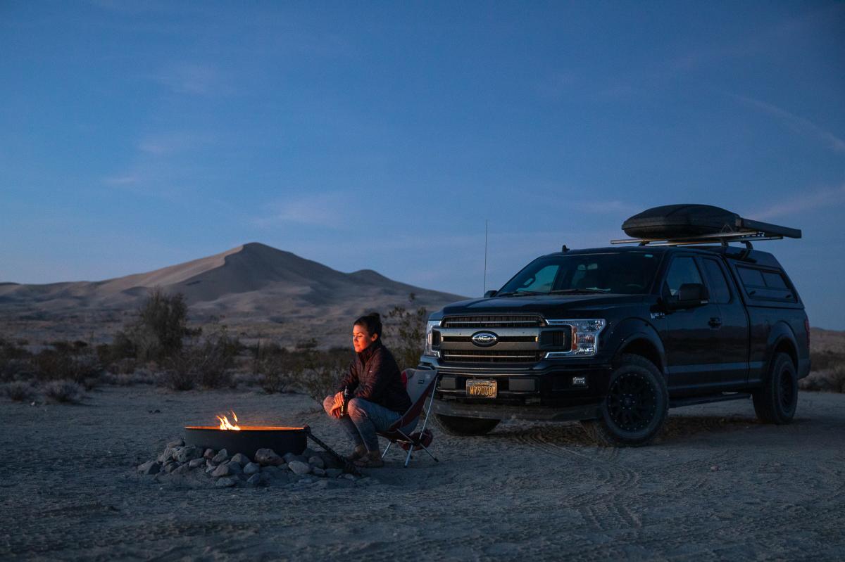 A woman sits by a campfire while camping at the Kelso Dunes in the Mojave National Preserve