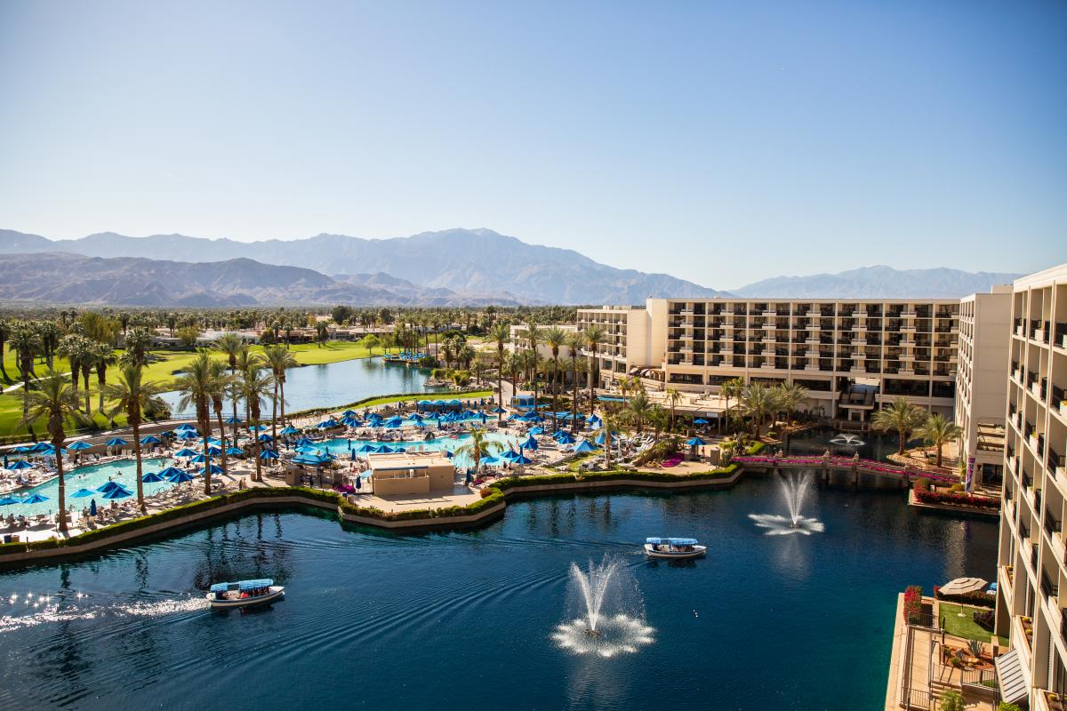 Aerial view of lake by resort and mountains in background with blue sky