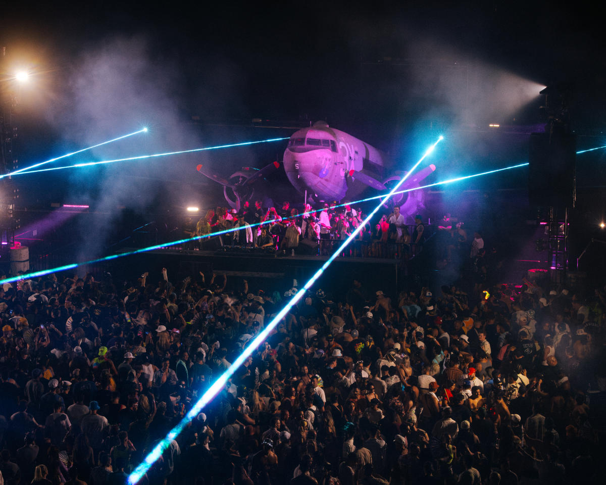 A big crowd of people gather at the Palm Springs Air Museum for an after hours party to listen to music with a huge airplane in the background.