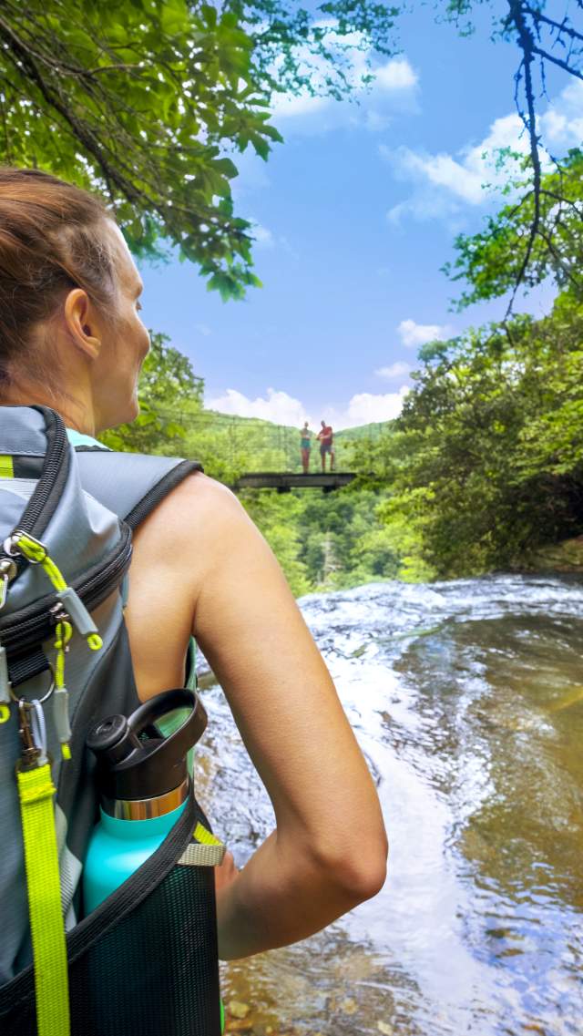 A hiker stands at Matthews Creek at Caesars Head State Park, looking at the wilderness bridge overlooking Raven Cliff Falls