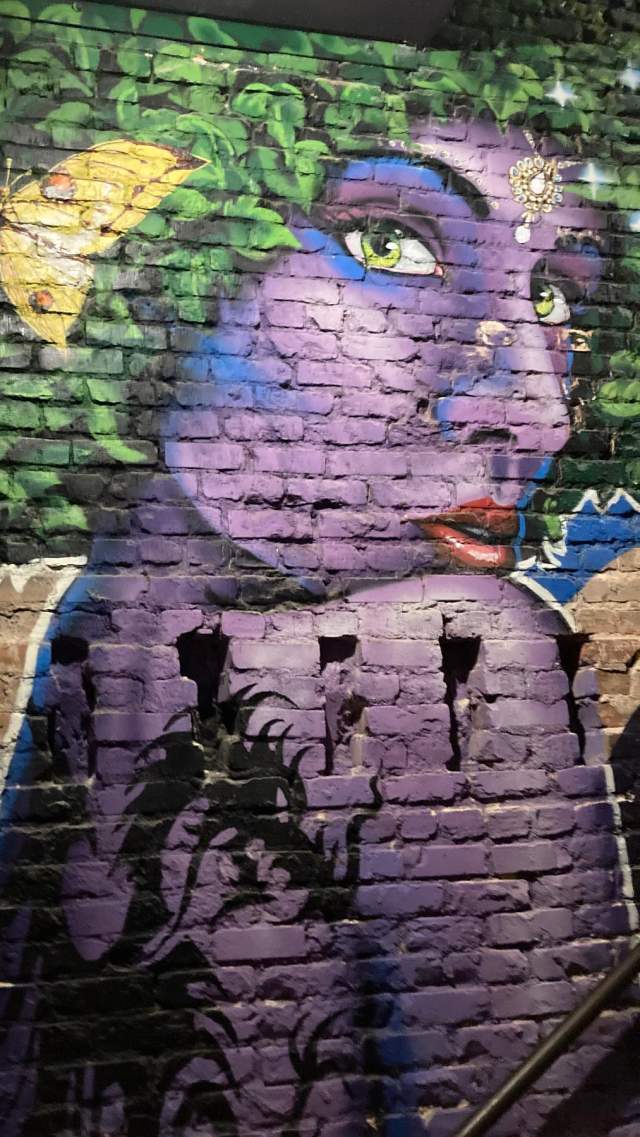 A wall mural of a purple girl with green leaves for hair and a yellow butterfly in it at Eden Rooftop Lounge in downtown Greenville, SC.