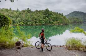 Man wearing helmet and cycling gear with a bike in front of a lake.