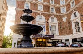 A water fountain in the foreground with the historic Westin Poinsett Hotel in the background, illuminated by the soft light of the rising sun.
