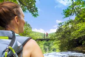 A hiker stands at Matthews Creek at Caesars Head State Park, looking at the wilderness bridge overlooking Raven Cliff Falls