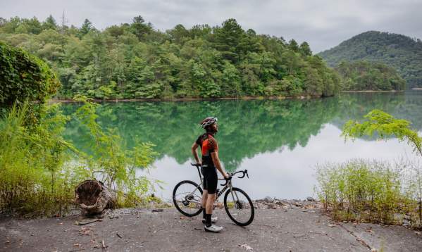 Man wearing helmet and cycling gear with a bike in front of a lake.
