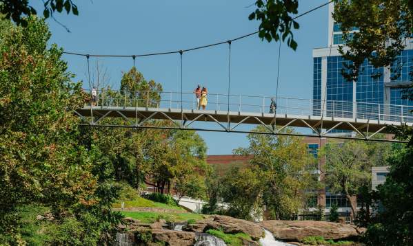 The Liberty Bridge at Falls Park on the Reedy and the view of the waterfalls below and some of the cityscape peeking out from behind the surrounding foliage.