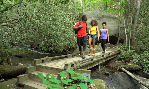 Three people walking along bridge while hiking