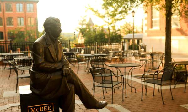 A bronze statue of a Vardry McBee, framed by the golden hues of a sunrise in the background.
