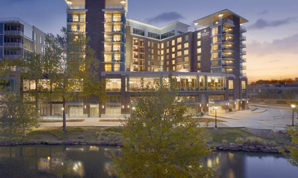 The Embassy Suites by Hilton in downtown Greenville, viewed from across the Reedy River, with the hotel’s modern exterior reflecting in the water.