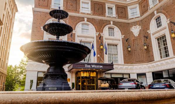 A water fountain in the foreground with the historic Westin Poinsett Hotel in the background, illuminated by the soft light of the rising sun.