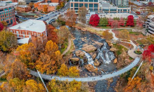 Classic autumn view of Liberty Bridge over the waterfall with Falls Tower, the downtown Greenville skyline, and Paris Mountain in the distance.