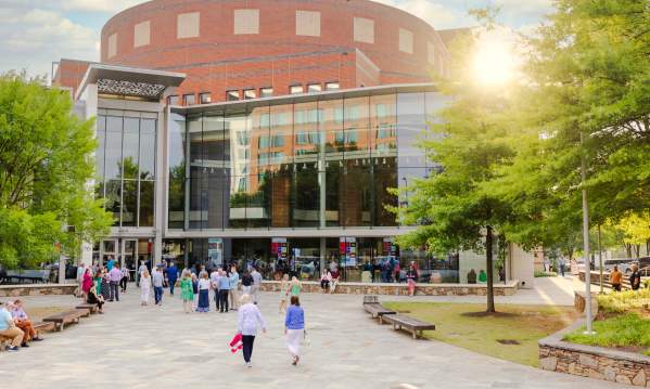 The Peace Center in downtown Greenville illuminated by the warm light of the setting sun, as people walk toward the building's glass entrance under a vibrant sky.