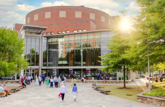 The Peace Center in downtown Greenville illuminated by the warm light of the setting sun, as people walk toward the building's glass entrance under a vibrant sky.