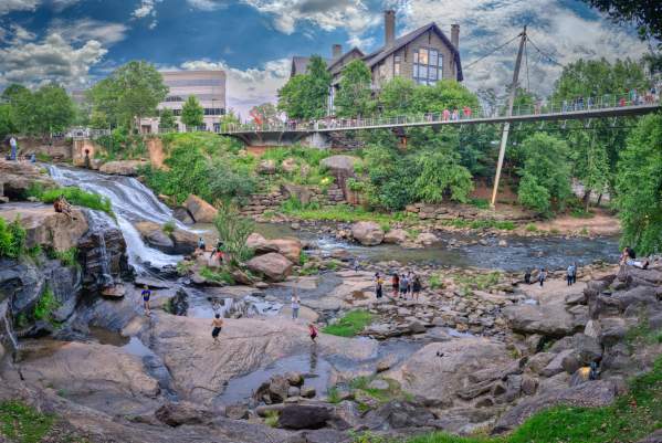 Visitors and residents of Greenville, SC play on the rocks and boulders in the Reedy River below the Liberty Bridge in Falls Park on the Reedy.