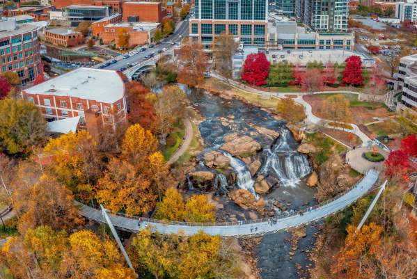 Classic autumn view of Liberty Bridge over the waterfall with Falls Tower, the downtown Greenville skyline, and Paris Mountain in the distance.