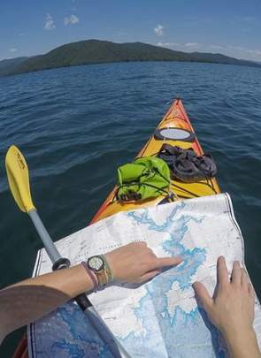 A view of a man in a kayak on a lake navigating his way to Laurel Creek Falls with a map
