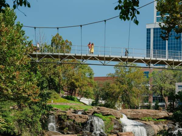 The Liberty Bridge at Falls Park on the Reedy and the view of the waterfalls below and some of the cityscape peeking out from behind the surrounding foliage.