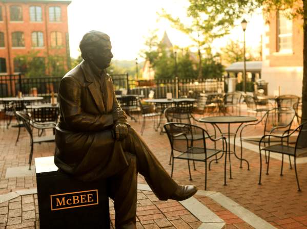 A bronze statue of a Vardry McBee, framed by the golden hues of a sunrise in the background.