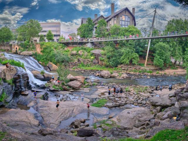 Visitors and residents of Greenville, SC play on the rocks and boulders in the Reedy River below the Liberty Bridge in Falls Park on the Reedy.