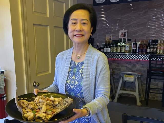 A photo of Alva Mak, owner of Asia Pacific Supermarket & Restaurant in Greenville, SC, holding a Chinese chicken dish.