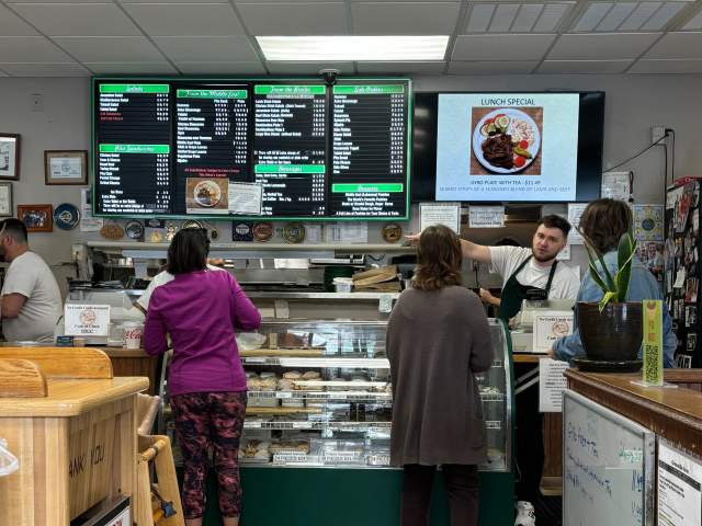 The interior of Pita House where two customers are in line at the glass deli counter to order.