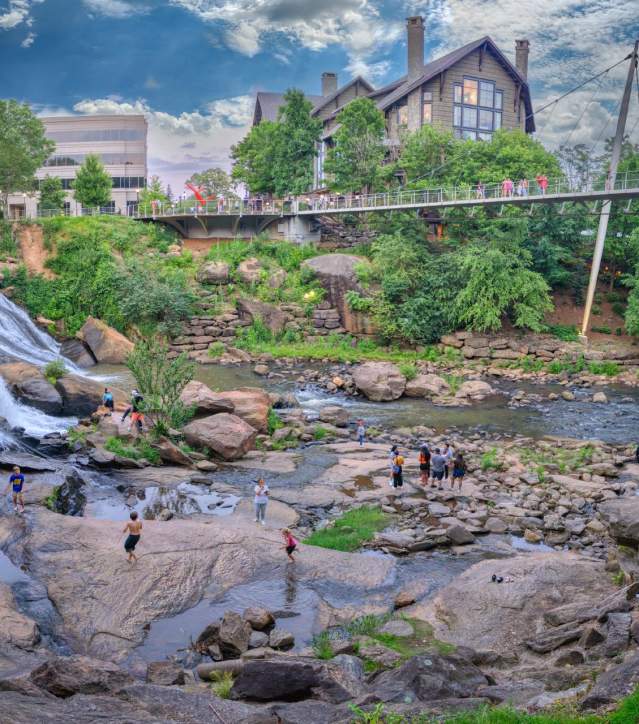Visitors and residents of Greenville, SC play on the rocks and boulders in the Reedy River below the Liberty Bridge in Falls Park on the Reedy.