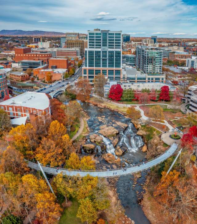 Classic autumn view of Liberty Bridge over the waterfall with Falls Tower, the downtown Greenville skyline, and Paris Mountain in the distance.