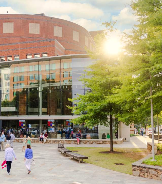 The Peace Center in downtown Greenville illuminated by the warm light of the setting sun, as people walk toward the building's glass entrance under a vibrant sky.