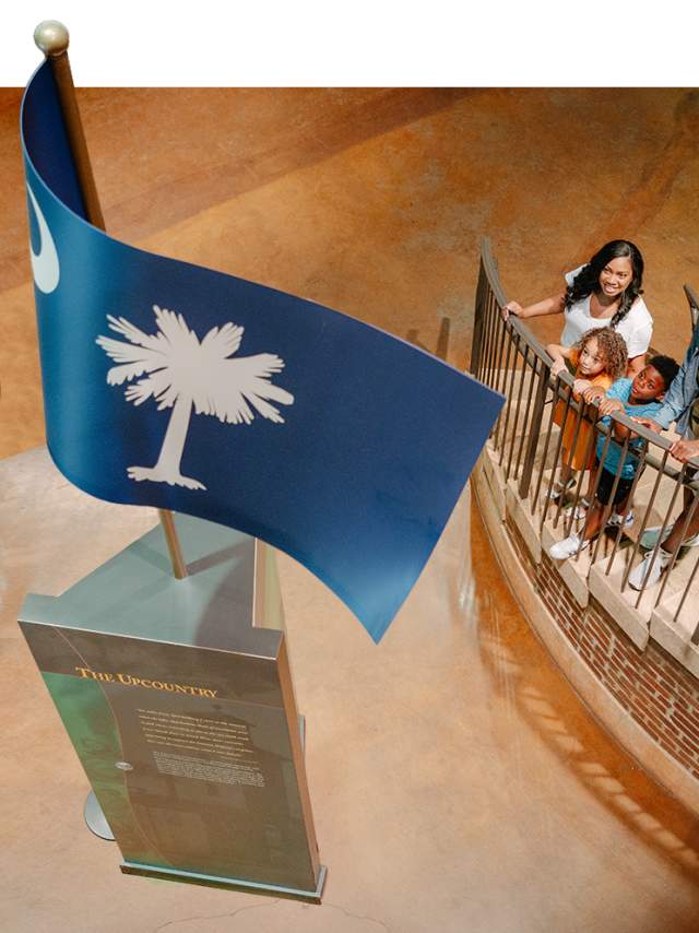 Family on stairs at the Upcountry History Museum admiring the South Carolina flag monument.