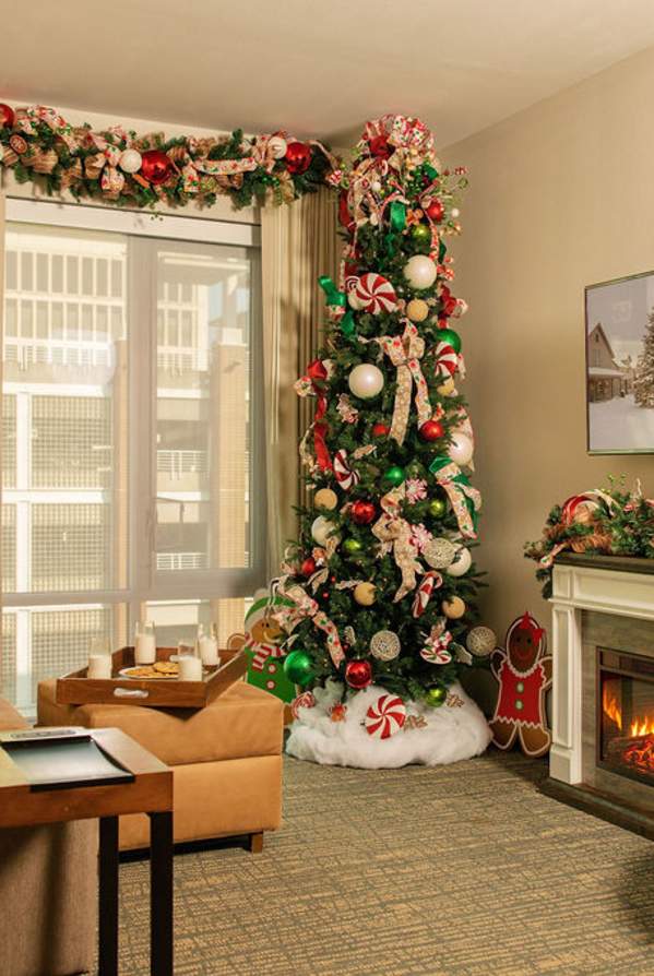 A cozy hotel room is decorated for Christmas with a tree and garland in the foreground, and a fireplace with a festive scene on the television in the background.