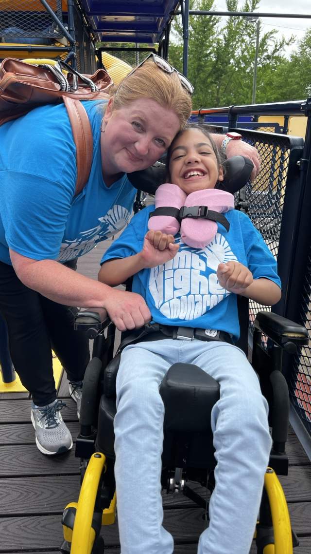 Woman smiling next to youth in wheelchair on accessible playground at The Children's Museum of the Upstate in Greenville, SC.