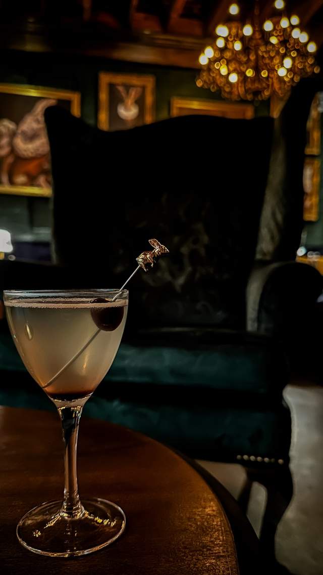 A lone cocktail sits amongst books in the cozy atmosphere of The Library at The Rabbit Hole in the Village of West Greenville, SC.