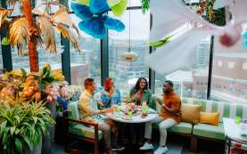 Group of four adults enjoying cocktails and food at Juniper, a uniquely decorated rooftop restaurant overlooking Downtown Greenville, SC.