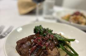 Steak dinner at Maestro Bistro with a glass of red wine in the background