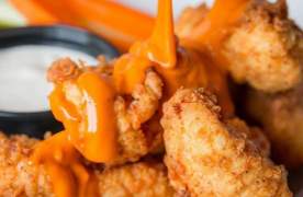 Chicken tenders on a plate with buffalo sauce being drizzled on them at Carolina Ale House