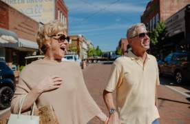 A cheerful older couple walking hand-in-hand along Greenville's Main Street, smiling and enjoying the vibrant downtown atmosphere.