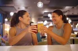 Two young women tapping glasses of beer together at a craft brewery in Greenville, SC.