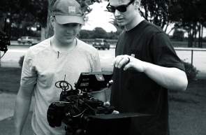 Two men working with a camera in a black and white photo.