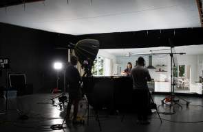 A film crew recording a woman cooking in the large 3,000 sq. ft. studio at Pronk Studios with dark walls except for the LED background wall, which features an LED image of a bright white home kitchen.