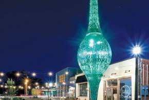 The Spindle sculpture lit up in a greenish aqua hue at night in The Village, a western area of Greenville, SC.