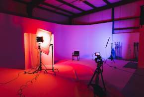 Red and purple lights creating a gradient background for photographers at the studio space at Kings Collective with camera equipment and a chair for a subject to sit.